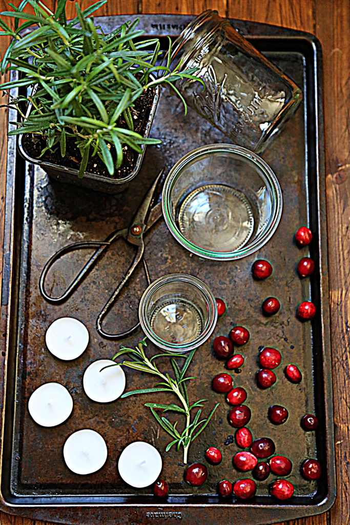 baking sheet with rosemary plan, glass jars, scissors, cranberries, tea lights. 