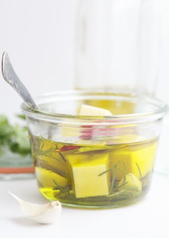 small glass jar of marinating cheese and herbs in olive oil