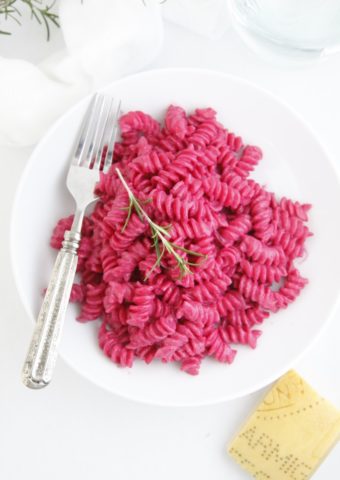 Pasta with Creamy Roasted Beet Sauce in white bowl with fork and wedge of Parmiggiano cheese to side