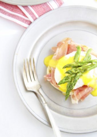 eggs benedict with asparagus on top on pewter plate with fork.