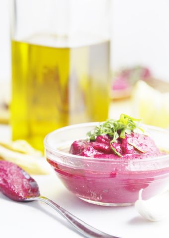 Roasted Red Beet Hummus in clear bowl with olive oil in background.