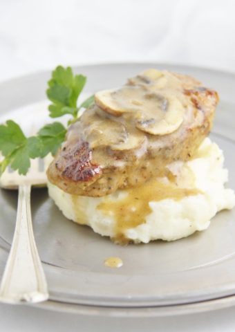 silver plate with pork medallions and sauce over a bed of mashed potatoes.