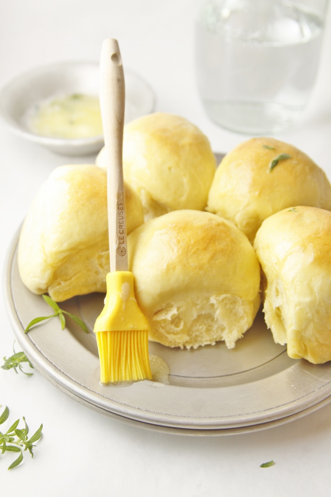 Light and Buttery Yeast Rolls on silver plate with silicon pastry brush. Bowl of butter behind.