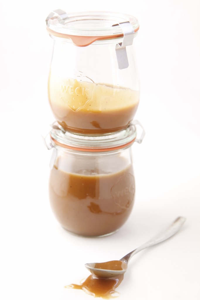 Two small glass jars of homemade Coffee Caramel Sauce stacked on each other. Spoon to side. 