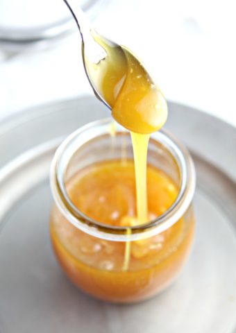 spoon going into glass jar of caramel sauce that is sitting on pewter plate.