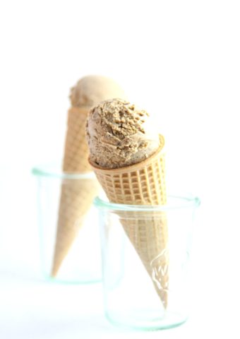 Ice cream cone with espresso ice cream being held in small glass jar. A second identical ice cream cone in background.