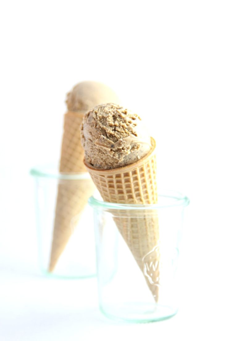 Ice cream cone with espresso ice cream being held in small glass jar. A second identical ice cream cone in background.