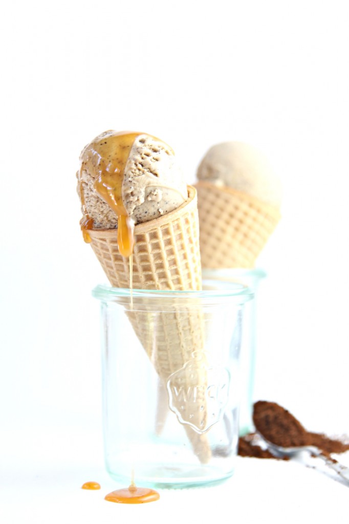 Espresso Ice Cream Cone with caramel sauce dripping off placed in small glass jar. Second ice cream cone visible in background. Spoon of espresso powder to right. 