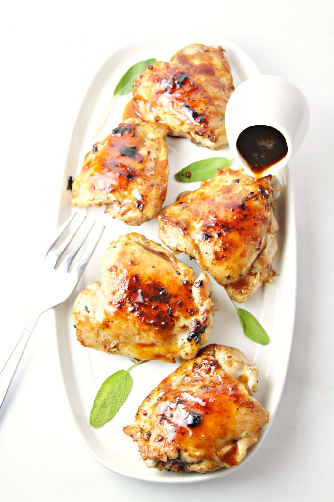 Cranberry Sage Glazed Grilled Chicken Thighs on white platter with fork and jar of sauce pouring over chicken. 