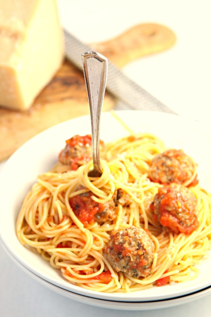 Spaghetti and Meatballs in white bowl. Wedge of parm behind.