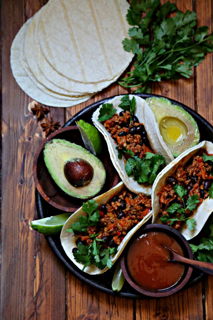 Black bean turkey tacos on brown plate with avocao and salsa. Tortillas behind. 
