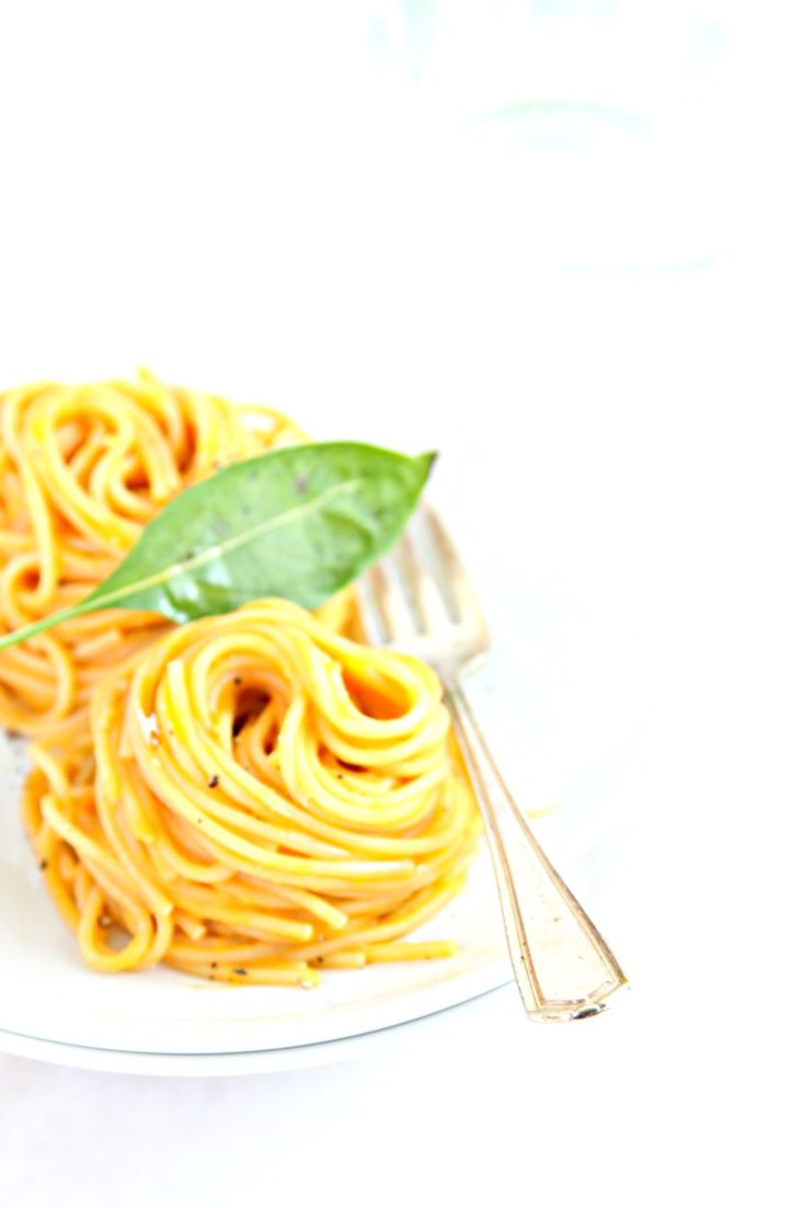 spaghetti nests on white plate with basil.