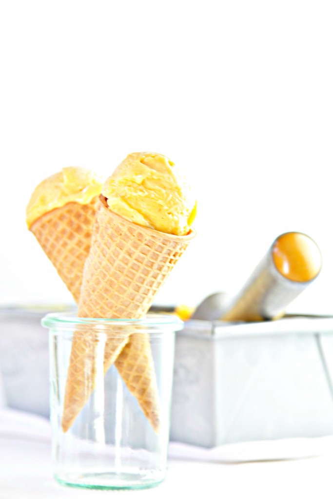 2 cones of Mango Lime Chili Ice Cream standing in glass jar. Loaf pan with ice cream and ice cream scooper behind.