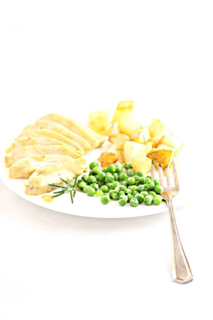 Maple Dijon Cicken sliced on white plate with fork and peas.