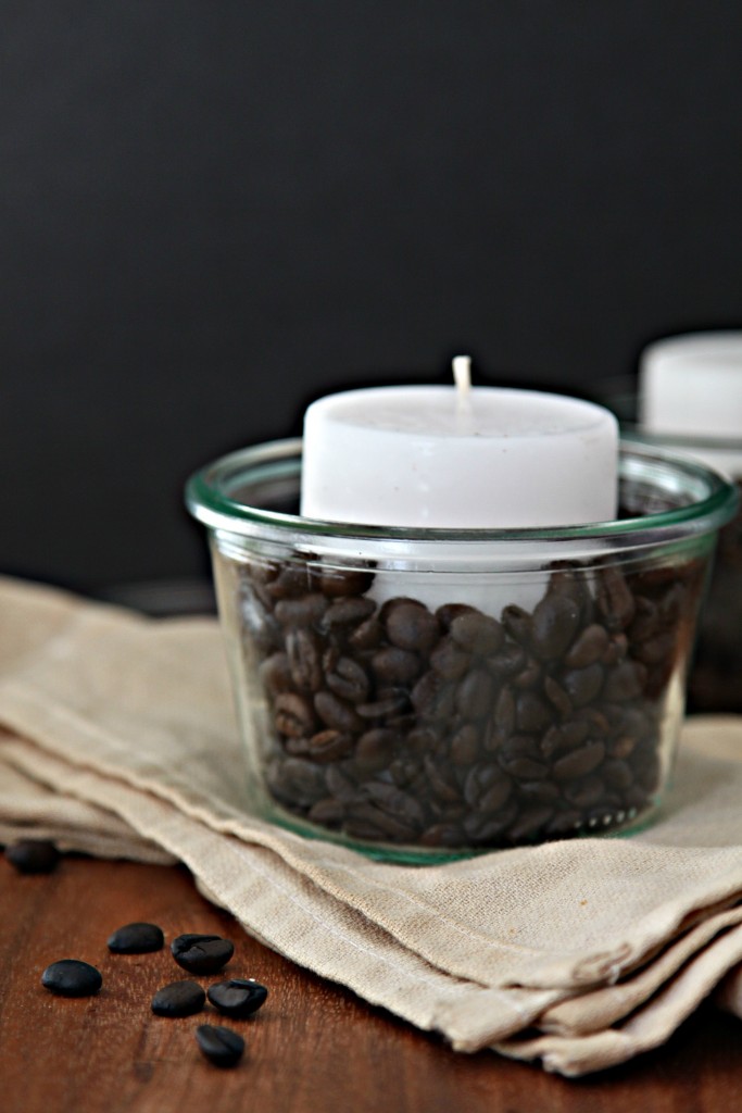 Glass jar with coffee Beans and votive candle. Jar is sitting on cloth napkin.