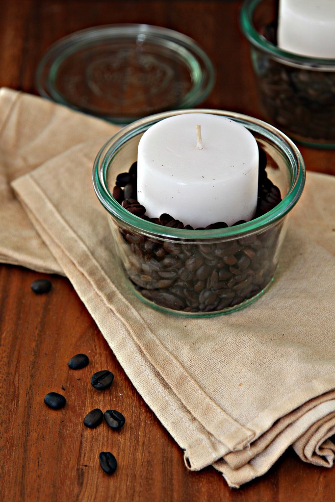Coffee Beans and votive candle in glass jar sitting on cloth napkin. Second candle partially visible in background.