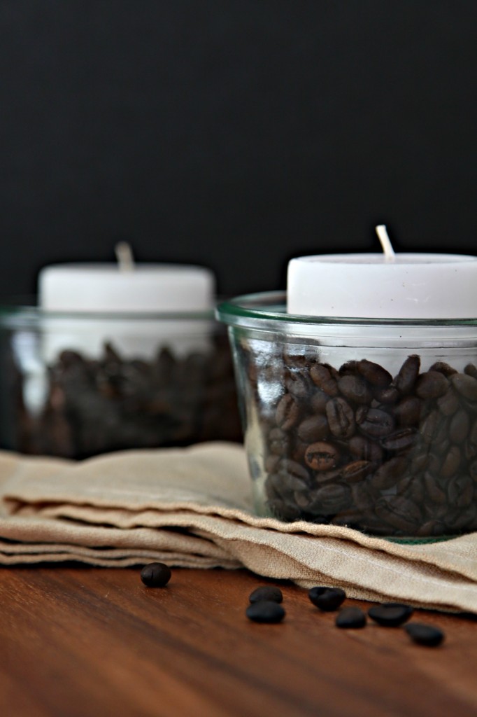glass jar with Coffee Beans and a white candle sitting on coffee stained cloth napkin.
