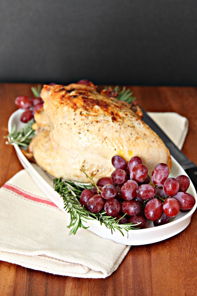 Roasted Turkey Breast with grapes and fresh rosemary surround it all sitting on white tray. Napkin under tray. 