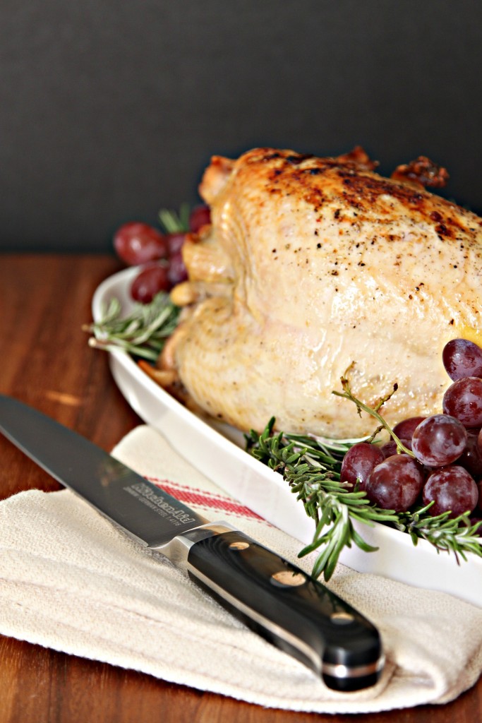 Roasted Turkey Breast on white tray with fresh grapes and rosemary for garnish. Knife and napkin in front of tray.