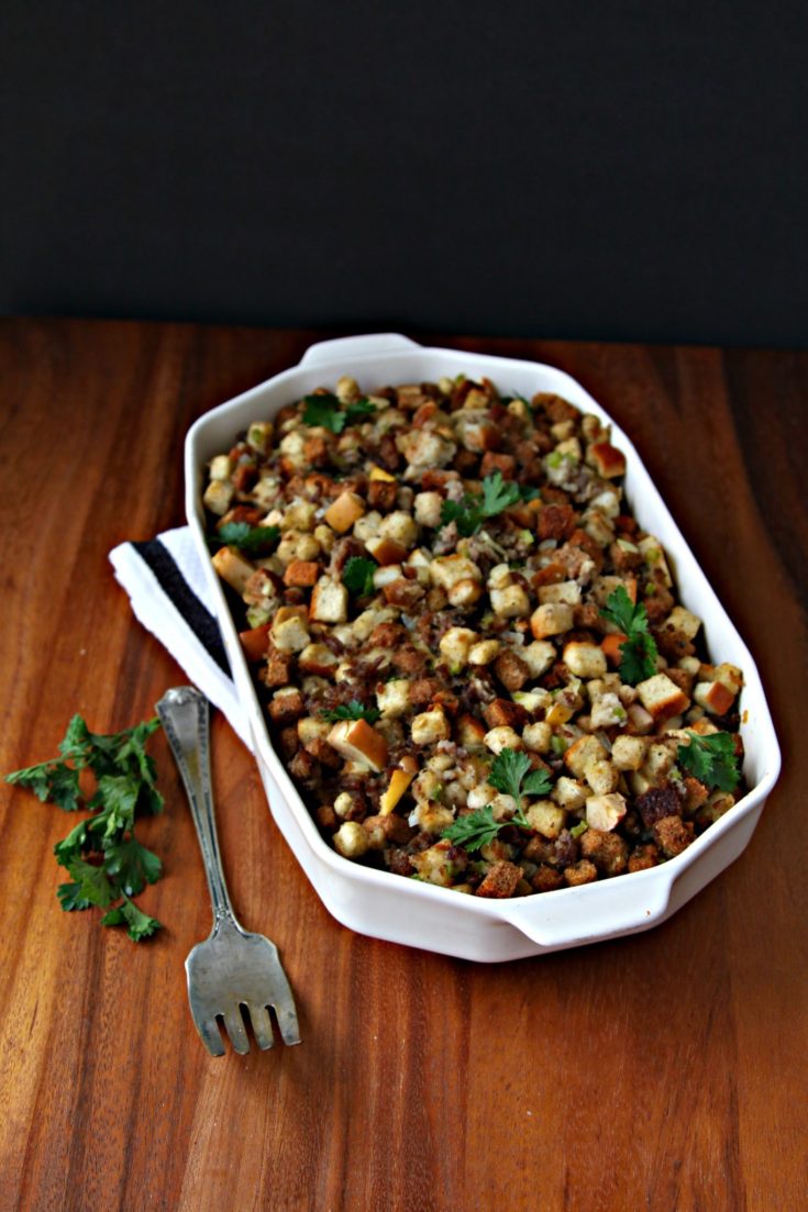 Sausage Apple and Herb Stuffing in white casserole dish. Serving utensil to side.