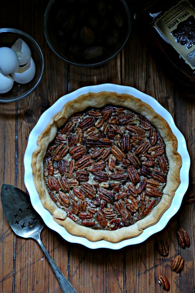 Bourbon Ginger Pecan Pie with egg shells, pecans, pie server and bourbon to side