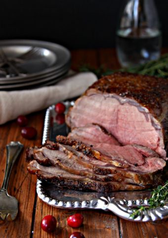 The Perfect Holiday Beef Roast on a silver platter sliced with plates surrounding