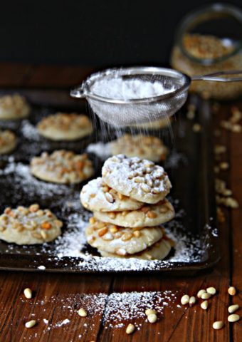 Pignoli Cookieson baking sheet with powdered sugar being shaken on top