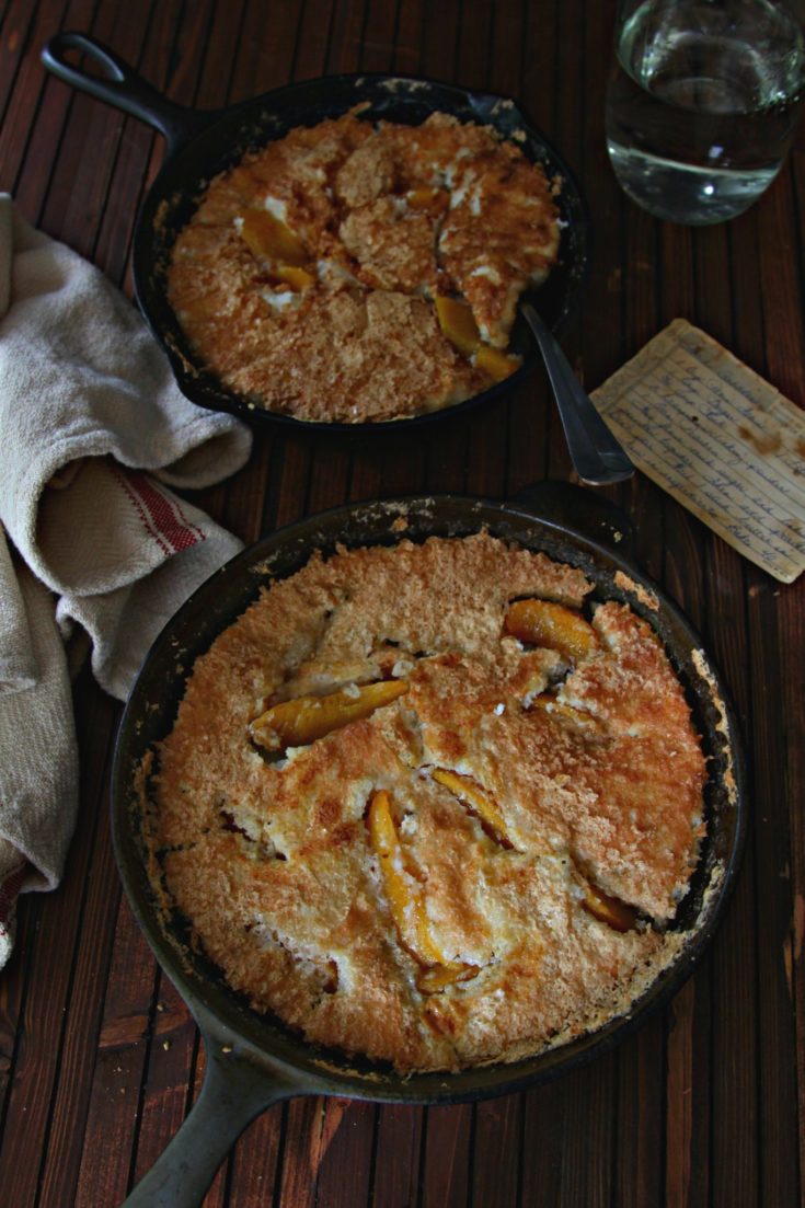 Peach Cobblers in black skillet with recipe card to side.