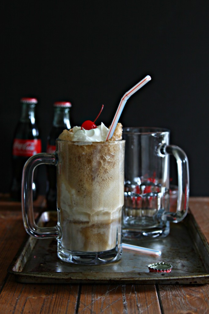 Glass mug of Bourbon Cherry Coke Float with straw on baking sheet. 2 bottles of coca-cola in background. 