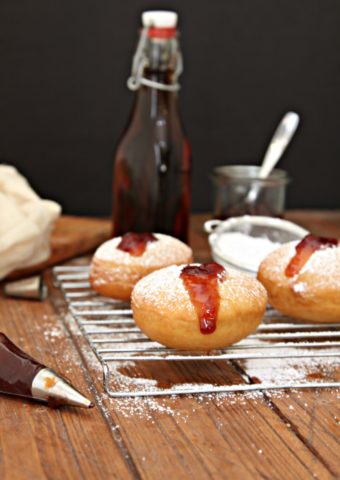 Bourbon Cherry Filled Doughnuts on a baking rack with bottle of extract to side and piping bag of cherry filling