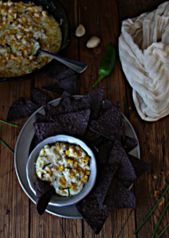 Spicy Corn Dip in silve bowl surrounded by blue corn chips on plate