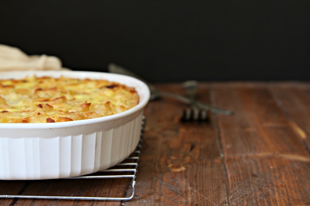 Baked Macaroni and Cheese in white casserole dish on cooling rack. Serving utensils to side. 