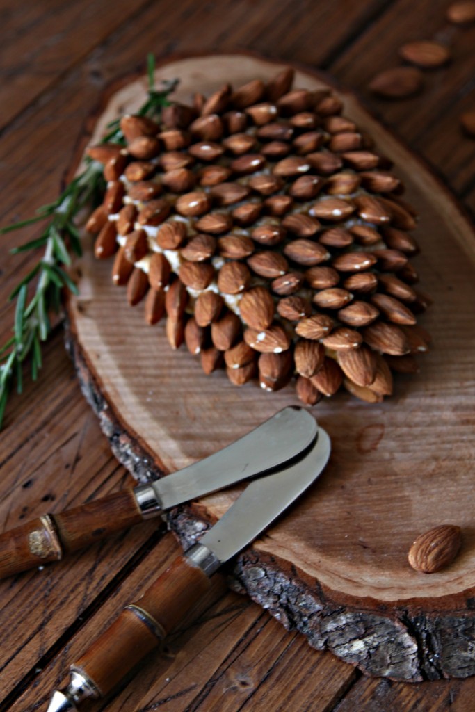 Pine Cone Shaped Holiday Cheese Ball on wood serving wedge with cheese spreaders to side. 