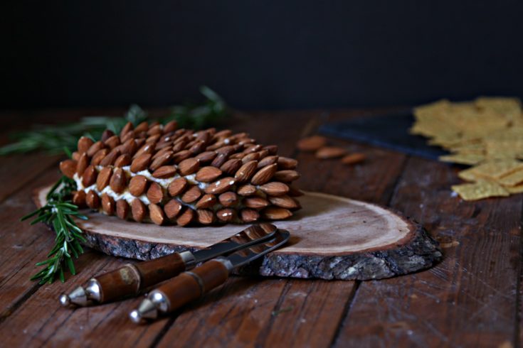 pine cone shaped holiday cheeseball on wood trivet with almonds and crackers to side