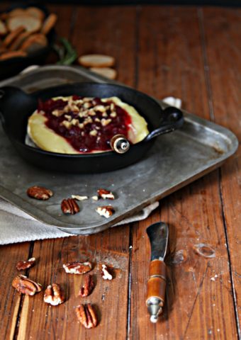 Baked Brie with Cranberries on baking sheet with scattered pecans and serving knife.