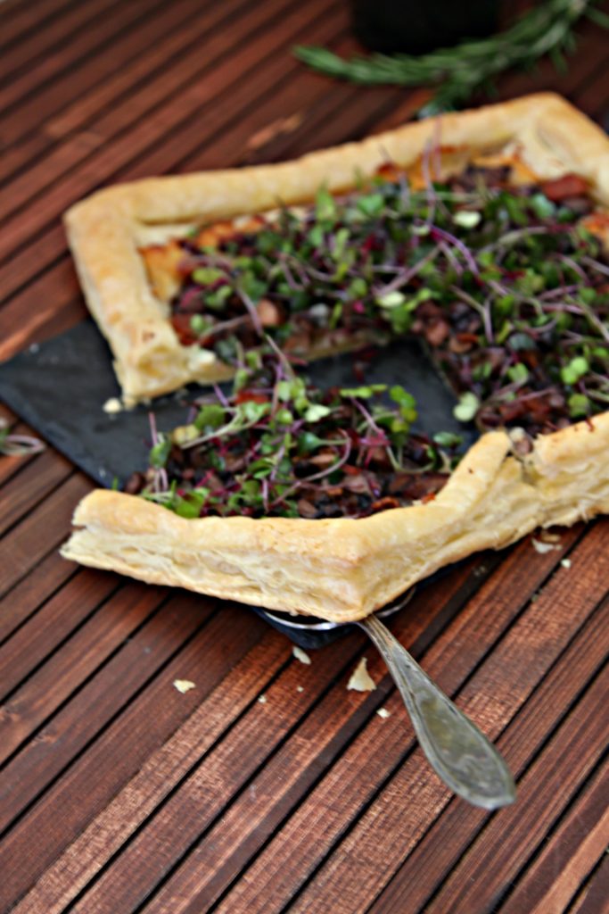 mushroom and bacon puff pastry tart served on a cheese slate pictured with wine bottle and rosemary sprig