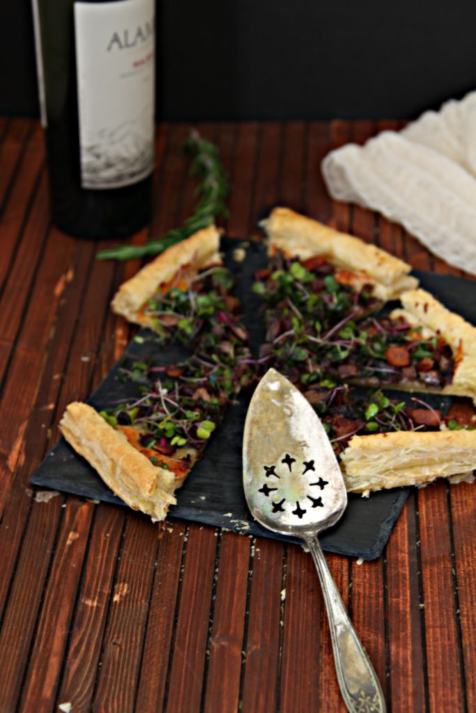 mushroom and bacon puff pastry tart served on a cheese slate pictured with wine bottle and rosemary sprig