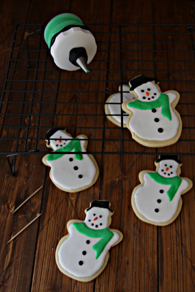 Snowman Sugar Cookies on baking rack with icing applicator. Toothpicks scattered. 