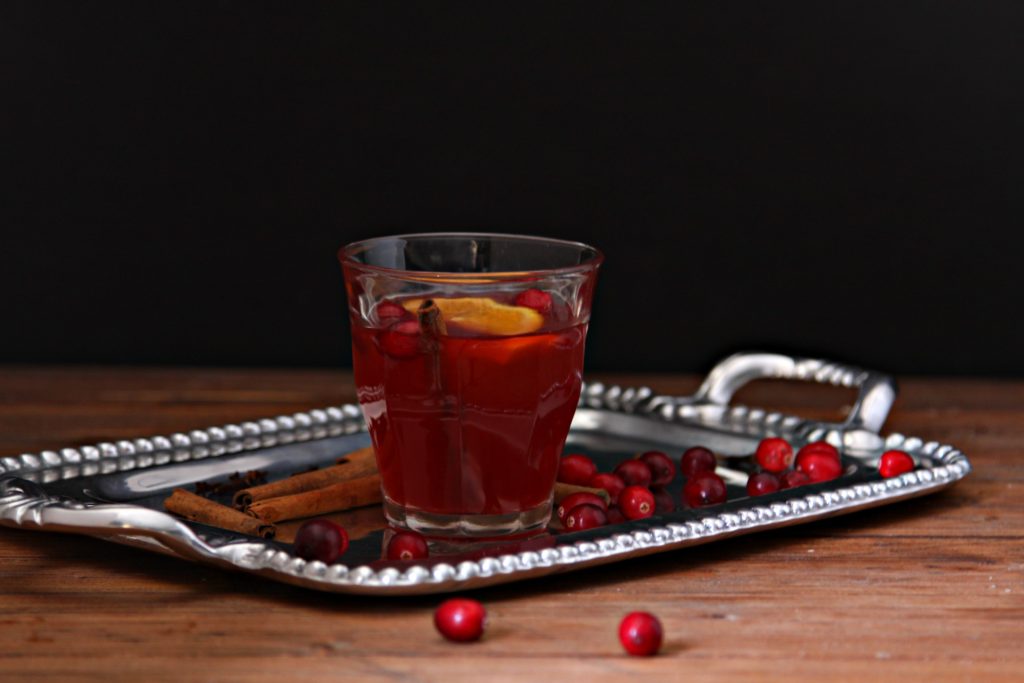 Slow Cooker Mulled Cranberry Punch in glass on silver tray. Cranberries scattered around glass.