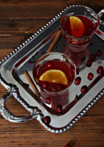 silver tray with two glasses of slow cooker cranberry punch. Cranberries and cinnamon sticks scattered around.
