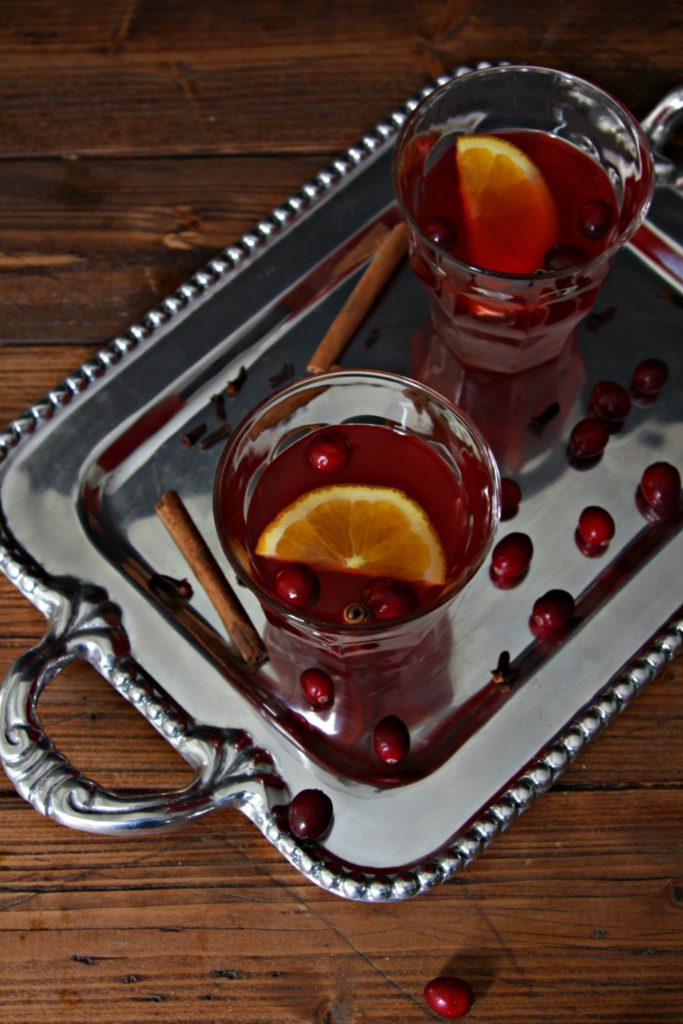 silver tray with two glasses of slow cooker cranberry punch. Cranberries and cinnamon sticks scattered around.