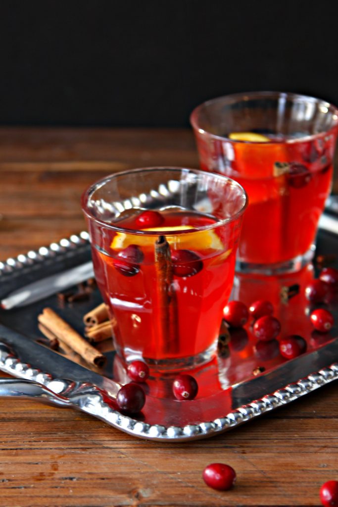 silver tray with two glasses of punch. Cinnamon sticks and cranberries scattered around glasses.
