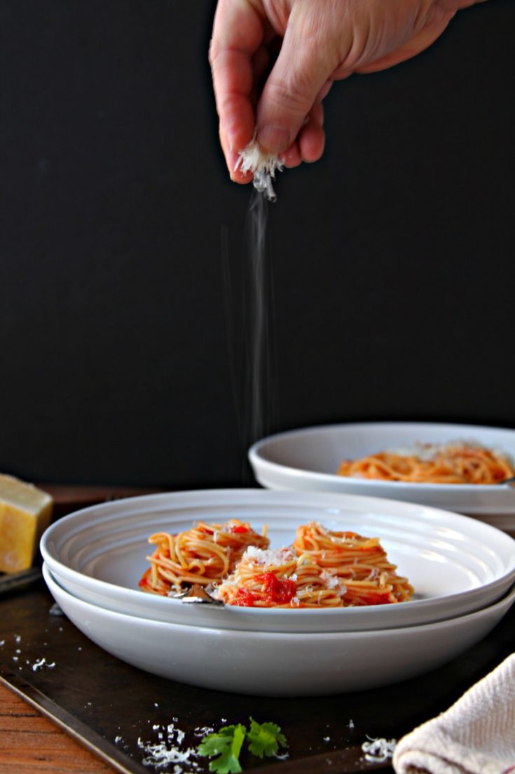 Spaghetti with Butter Roasted Tomato Sauce in white bowl. Hand sprinkling parmesan cheese onto bowl.