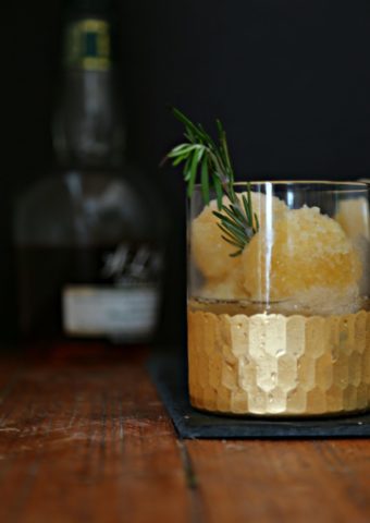 Bourbon Slush in glass with gold rim. Bottle of whiskey behind.