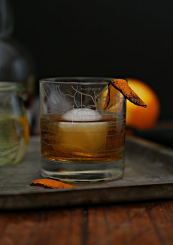 Old Fashioned cocktail in rocs glass with ice sphere on baking sheet