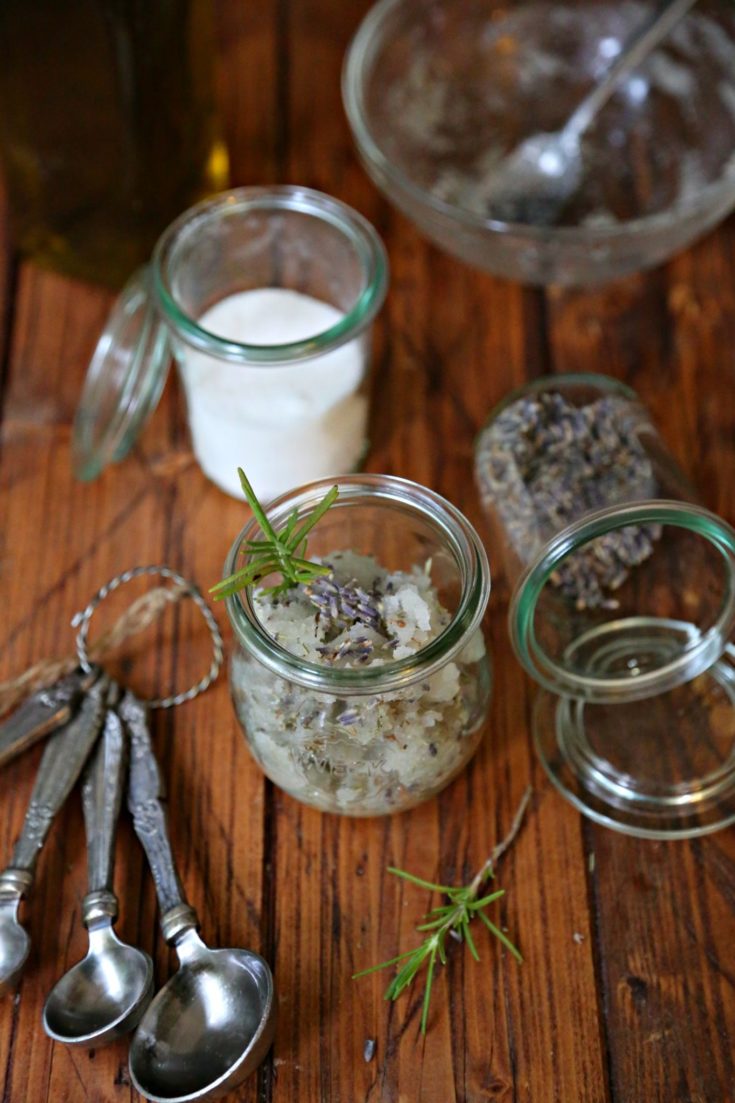 Rosemary Lavender Sugar Scrub in sall glass jars. Measurings spoons, jar of sugar and rosemary sprigs to side.