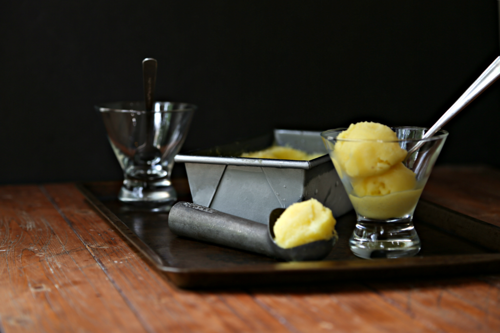 baking sheet with glasses of Pina Colada Sorbet, loaf pan with sorbet and ice cream scooper with sorbet. 