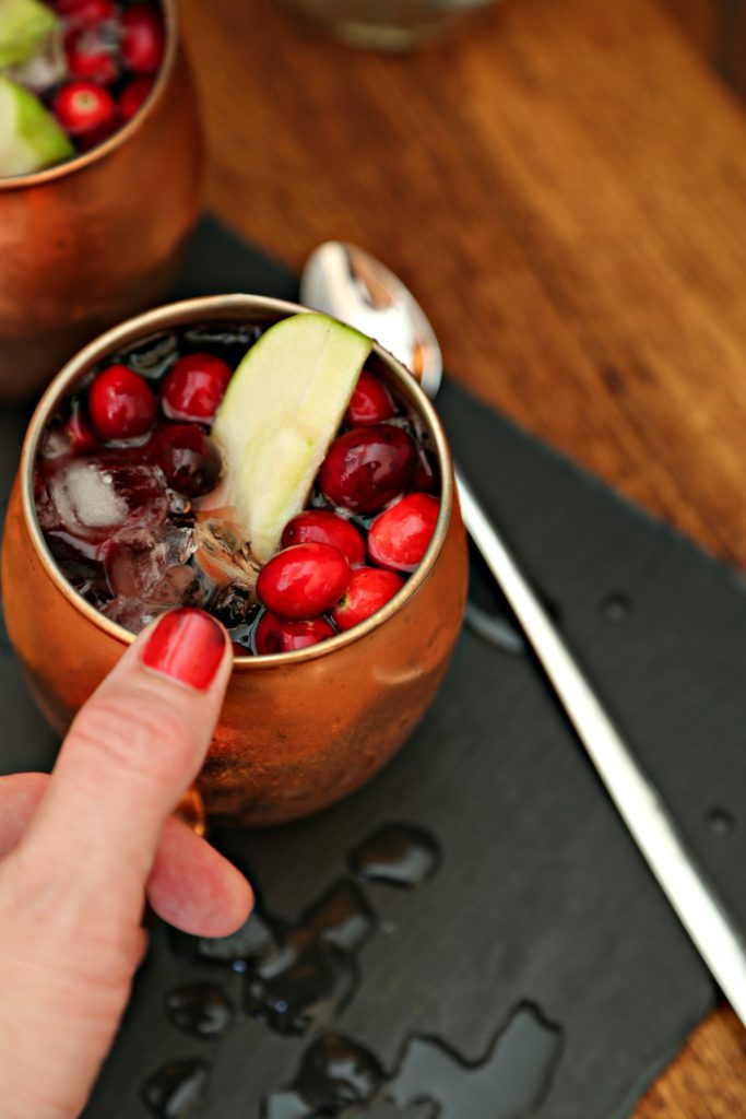 hand holding copper mug with cranberry apple Moscow mule. Spoon to side. 