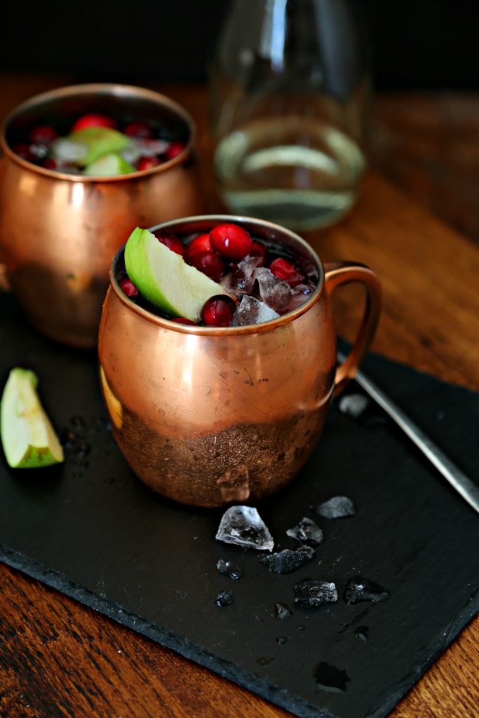 Cranberry Apple Moscow Mule cocktails in copper mugs on black slate.  