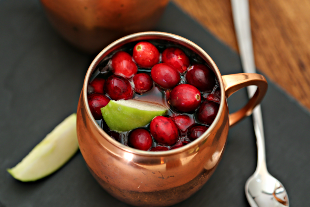 Cranberry Apple Moscow Mule in copper mug. Spoon and lime wedge to side. 
